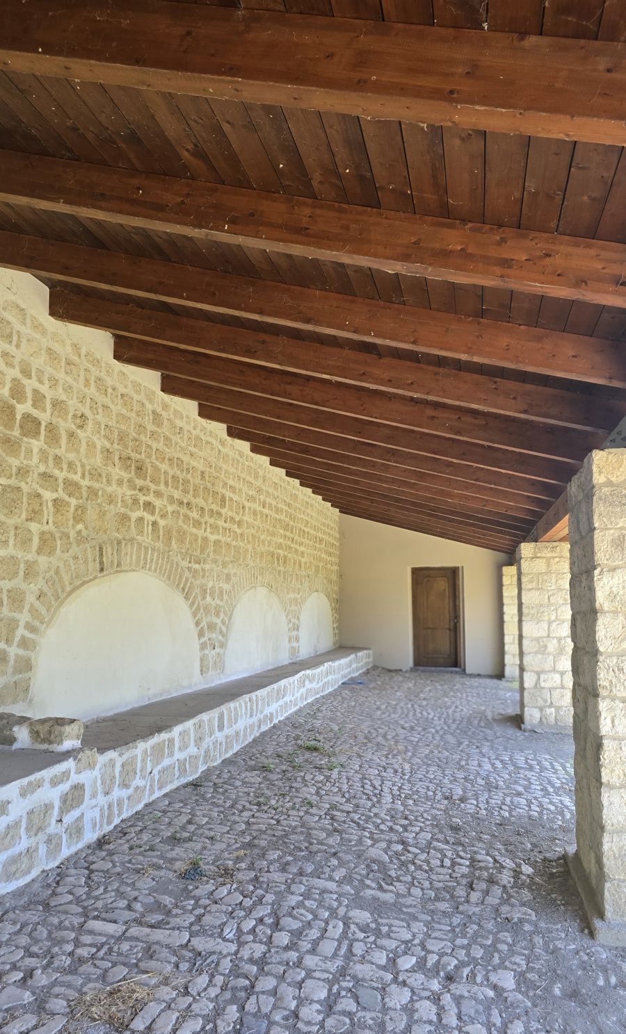 Il portico delle stalle con le mangiatoie ad arco, le travi in legno e il selciato in pietra